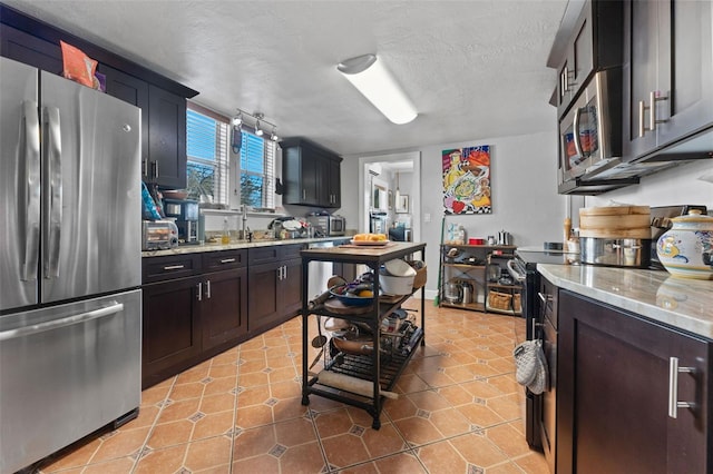 kitchen with light stone counters, a sink, a textured ceiling, stainless steel appliances, and light tile patterned floors