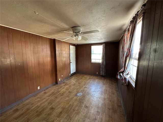 empty room with a textured ceiling, wooden walls, wood finished floors, a ceiling fan, and baseboards