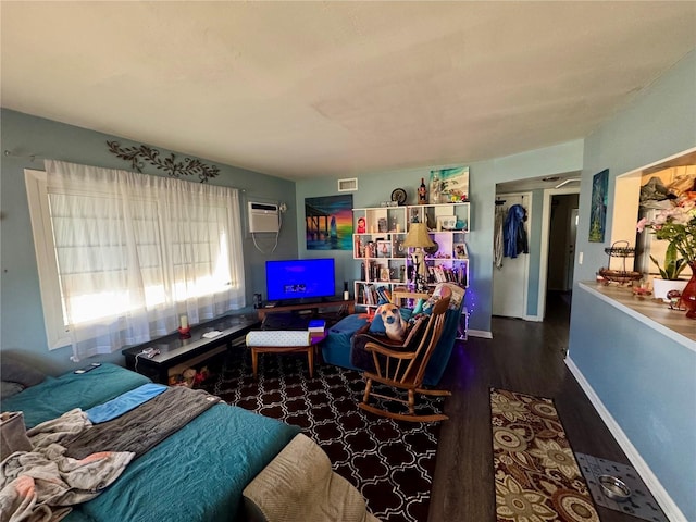 bedroom with a wall unit AC, baseboards, and wood finished floors