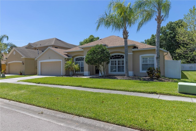 view of front of property with stucco siding, a front yard, fence, a garage, and driveway