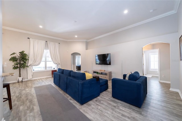 living room featuring a wealth of natural light, crown molding, arched walkways, and wood finished floors