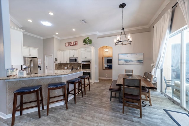 kitchen featuring light stone counters, arched walkways, stainless steel appliances, visible vents, and a kitchen bar