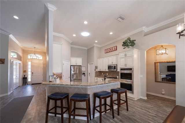 kitchen with crown molding, visible vents, backsplash, appliances with stainless steel finishes, and a kitchen breakfast bar