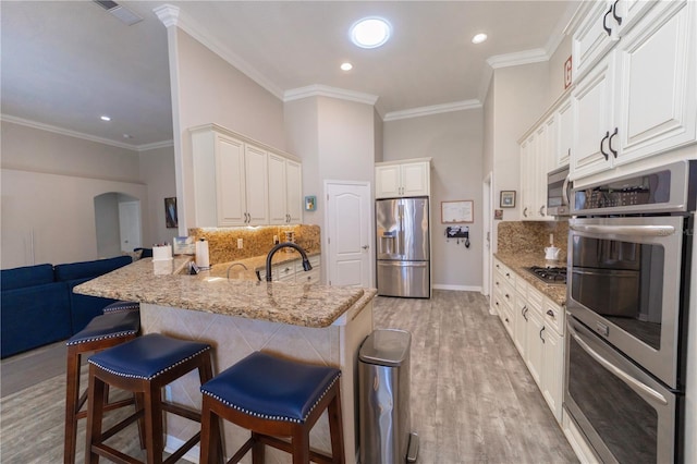 kitchen with arched walkways, a breakfast bar, stainless steel appliances, a sink, and a peninsula