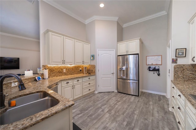 kitchen with a sink, light wood-type flooring, backsplash, stainless steel refrigerator with ice dispenser, and crown molding