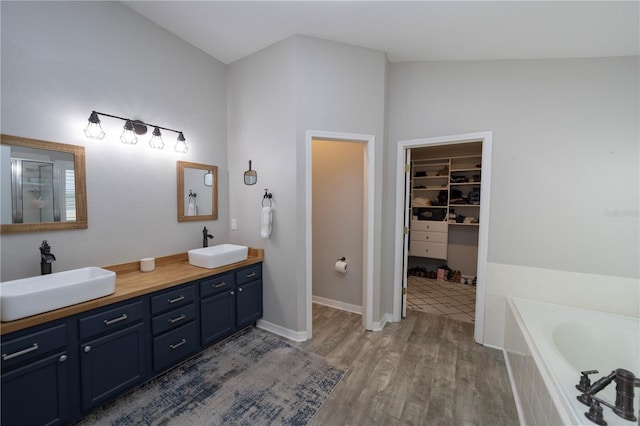 full bathroom with double vanity, a spacious closet, a sink, and wood finished floors