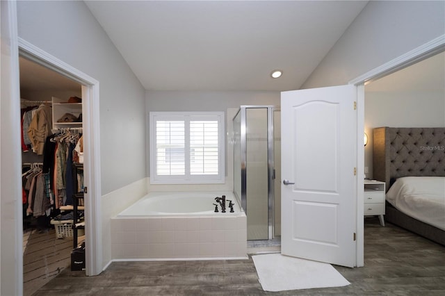 bathroom with a stall shower, lofted ceiling, wood finished floors, a garden tub, and a walk in closet