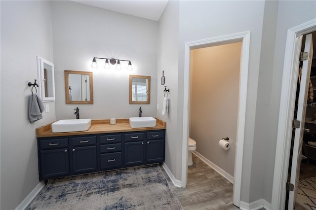 bathroom with toilet, double vanity, a sink, and wood finished floors