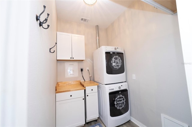 laundry room featuring stacked washing maching and dryer, baseboards, visible vents, and cabinet space