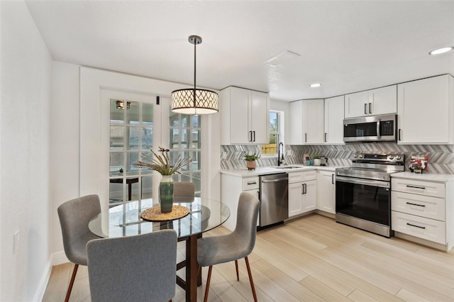 kitchen featuring stainless steel appliances, decorative backsplash, white cabinets, a sink, and light wood-type flooring