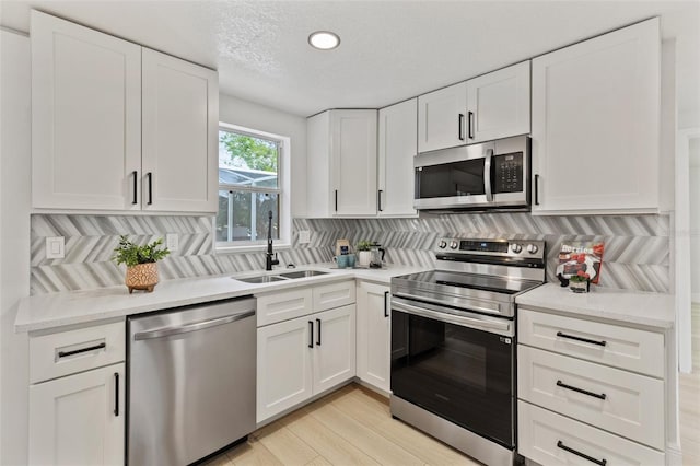 kitchen with light wood-style flooring, appliances with stainless steel finishes, a sink, white cabinetry, and backsplash