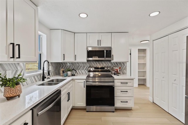 kitchen with stainless steel appliances, light stone counters, a sink, and white cabinetry