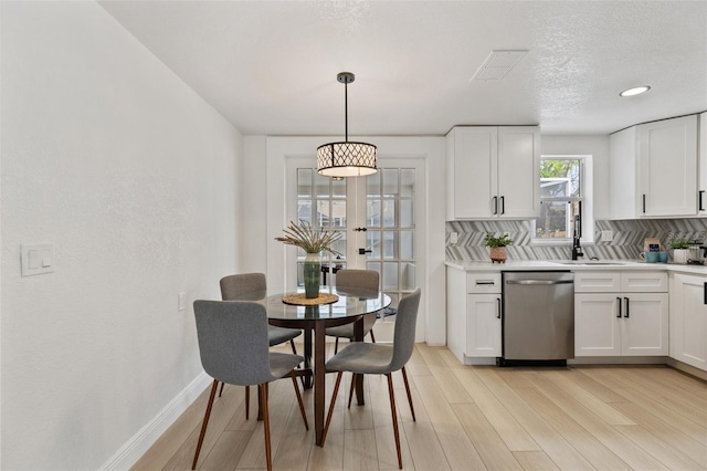 kitchen featuring light wood finished floors, stainless steel dishwasher, white cabinets, and tasteful backsplash