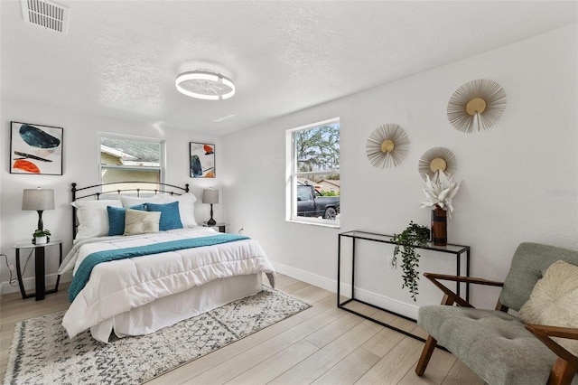 bedroom featuring light wood-type flooring, multiple windows, visible vents, and a textured ceiling