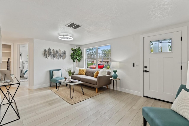 living area featuring a textured ceiling, light wood finished floors, visible vents, and baseboards