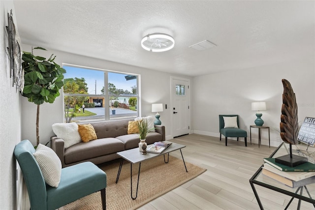 living area featuring light wood-type flooring, a textured ceiling, and baseboards