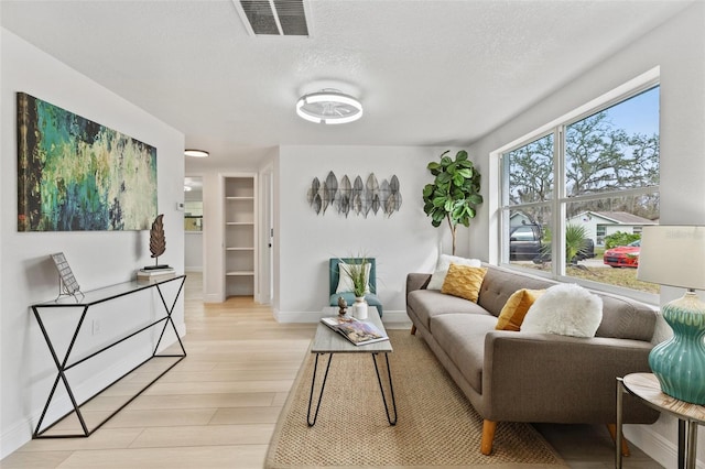 living area with light wood-type flooring, baseboards, visible vents, and a textured ceiling