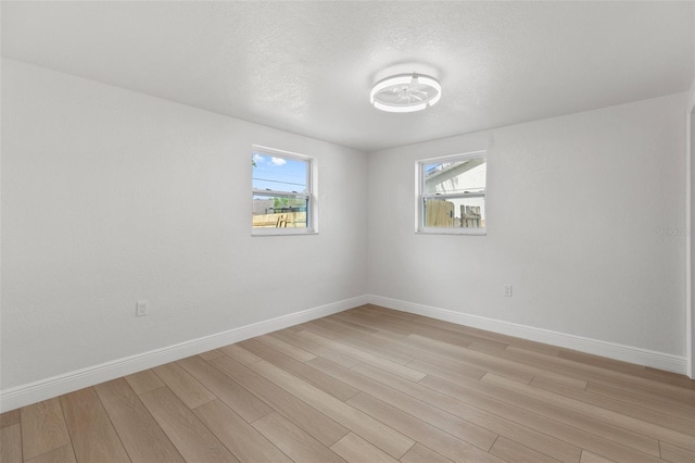 empty room with light wood-style floors, a textured ceiling, and baseboards