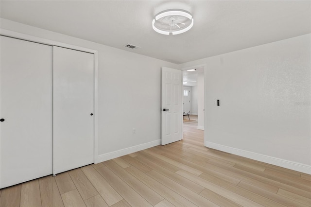 unfurnished bedroom featuring light wood-type flooring, a closet, visible vents, and baseboards