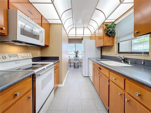 kitchen featuring light tile patterned floors, dark countertops, brown cabinetry, a sink, and white appliances