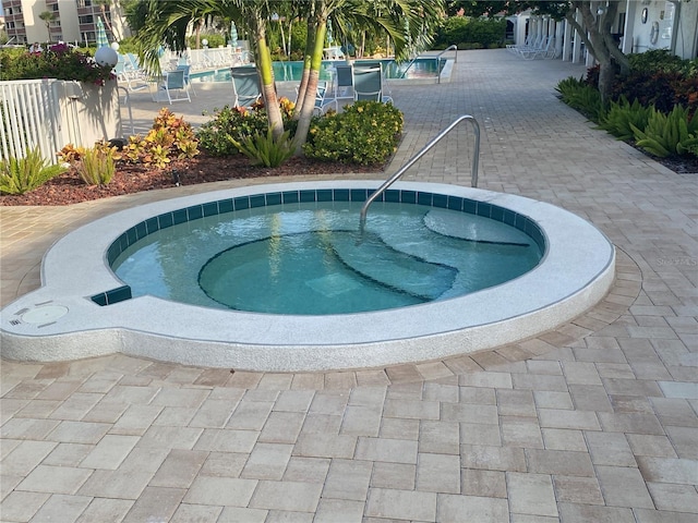 pool with a patio, fence, and a hot tub