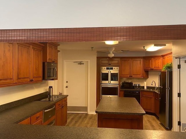 kitchen with dark countertops, black appliances, brown cabinetry, and a warming drawer