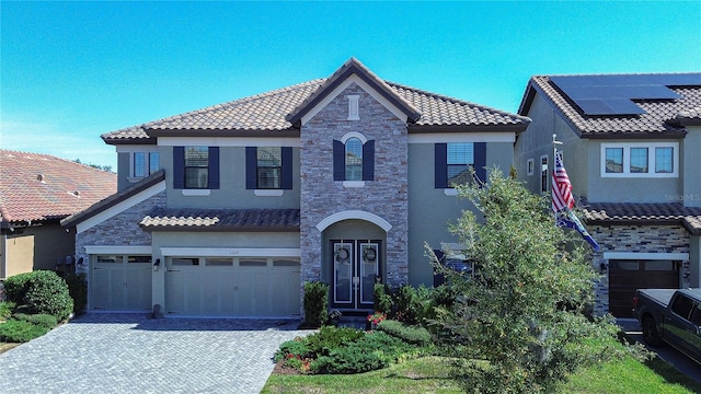 mediterranean / spanish-style home featuring stone siding, a tiled roof, decorative driveway, french doors, and roof mounted solar panels