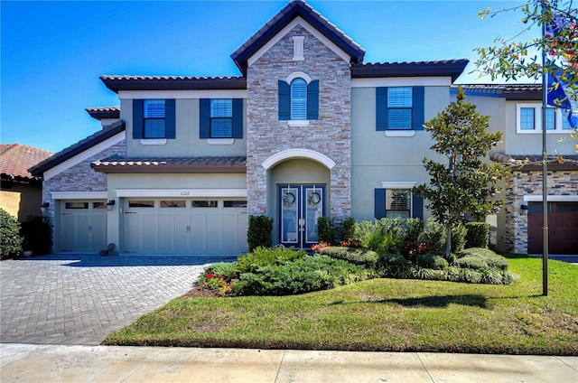 view of front of house with a garage, stone siding, decorative driveway, a front lawn, and stucco siding