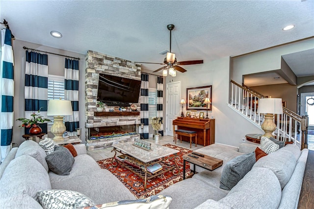 living room with a ceiling fan, a stone fireplace, a textured ceiling, wood finished floors, and stairs