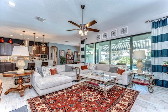 living area featuring arched walkways, visible vents, a ceiling fan, a textured ceiling, and light wood-type flooring