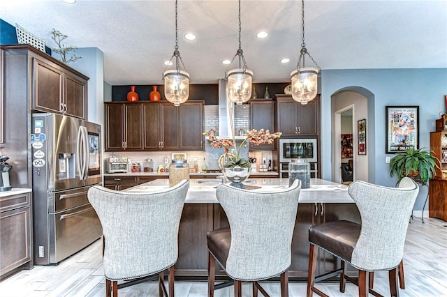 kitchen with arched walkways, light countertops, dark brown cabinets, built in microwave, and stainless steel fridge