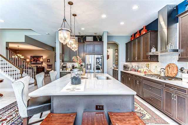 kitchen featuring arched walkways, a breakfast bar, wall chimney range hood, appliances with stainless steel finishes, and decorative backsplash