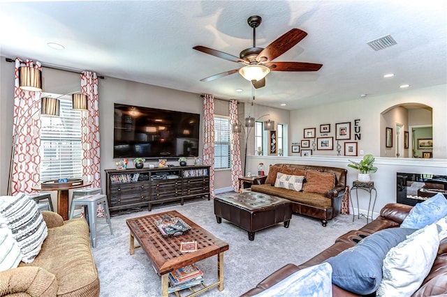 living room with a textured ceiling, carpet floors, visible vents, and a ceiling fan