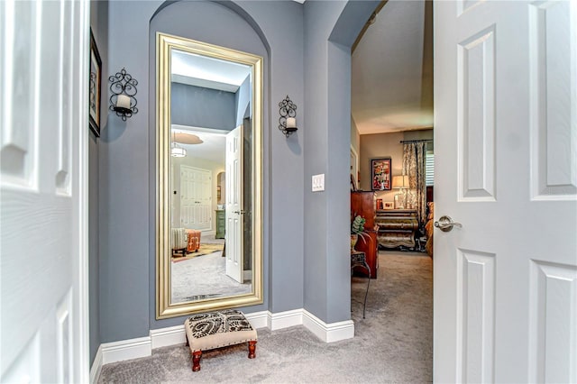 hallway featuring carpet, arched walkways, and baseboards