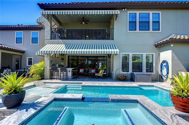 back of house with stucco siding, a pool with connected hot tub, a patio area, fence, and a balcony