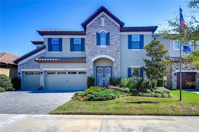 view of front facade with decorative driveway, a tile roof, stucco siding, an attached garage, and stone siding