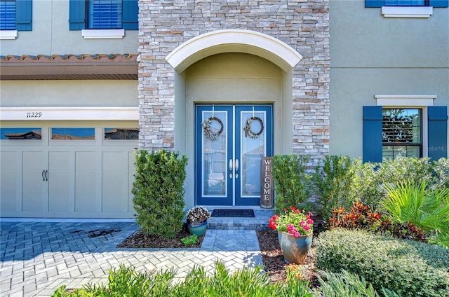 doorway to property with an attached garage, french doors, and stucco siding