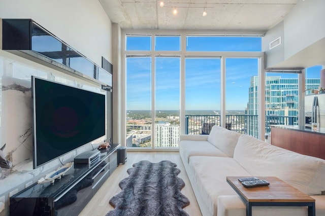 living room featuring a city view, floor to ceiling windows, visible vents, track lighting, and wood finished floors