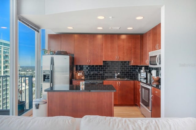 kitchen with stainless steel appliances, dark countertops, backsplash, a sink, and a kitchen island