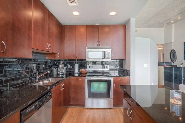 kitchen with visible vents, dark stone countertops, stainless steel appliances, light wood-type flooring, and a sink