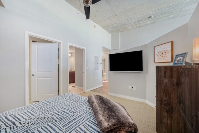 bedroom featuring a towering ceiling, ensuite bath, baseboards, and light colored carpet