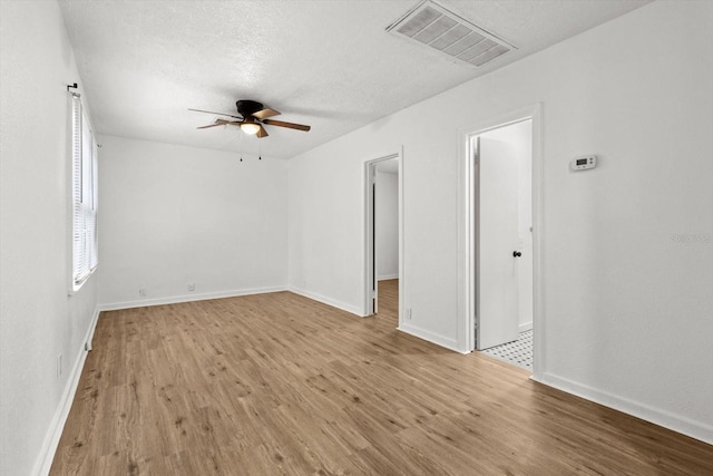 unfurnished room featuring baseboards, visible vents, ceiling fan, wood finished floors, and a textured ceiling