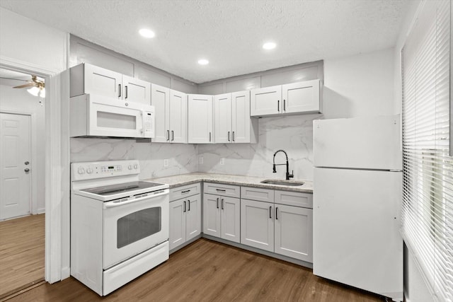 kitchen featuring dark wood finished floors, white appliances, a sink, and backsplash