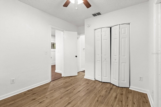 unfurnished bedroom featuring a closet, a textured ceiling, baseboards, and wood finished floors