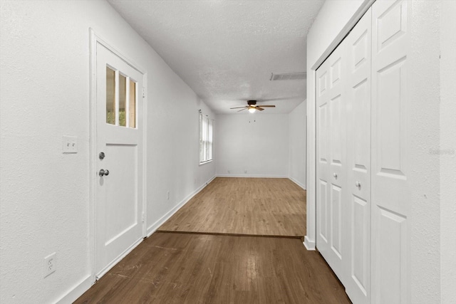 hallway with visible vents, a textured ceiling, baseboards, and dark wood-style flooring