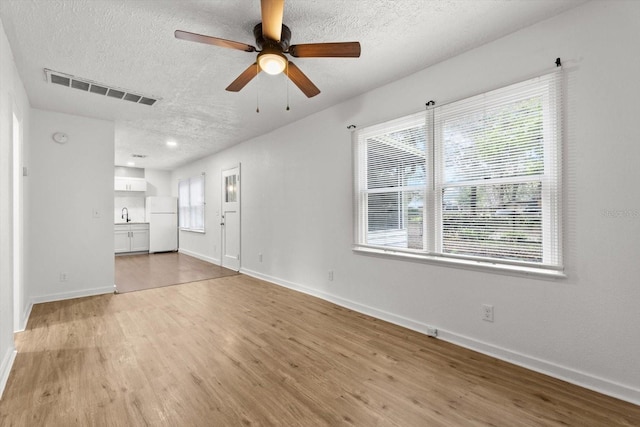 unfurnished living room featuring light wood-type flooring, visible vents, a textured ceiling, and baseboards