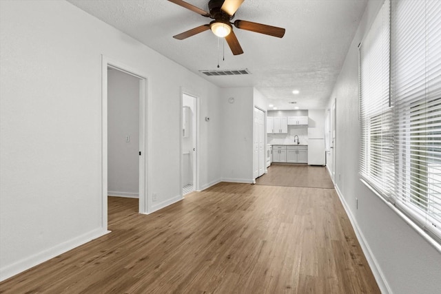 unfurnished living room with visible vents, light wood-style floors, a sink, a textured ceiling, and baseboards