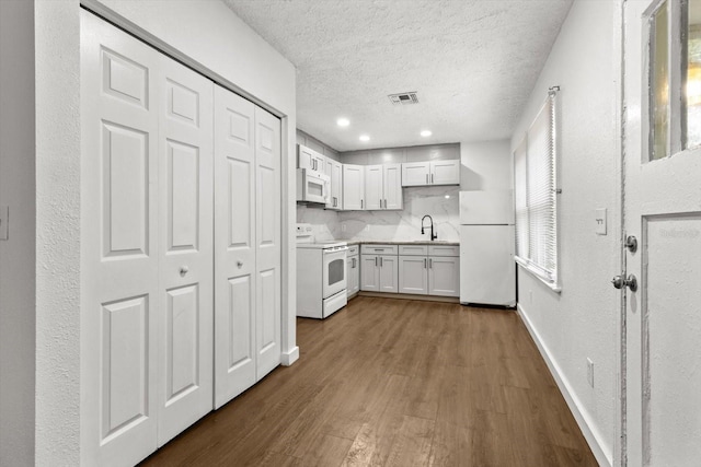 kitchen featuring a textured ceiling, white appliances, dark wood-style flooring, a sink, and light countertops