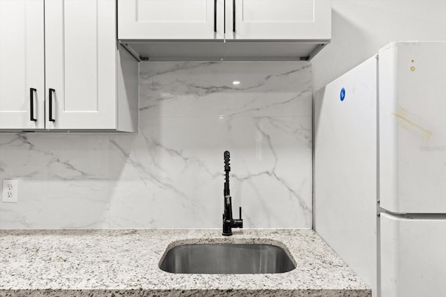 kitchen with light stone counters, decorative backsplash, freestanding refrigerator, white cabinetry, and a sink