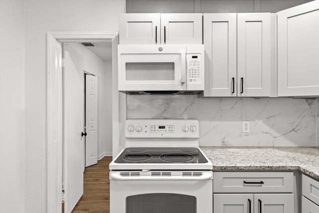 kitchen featuring white appliances, wood finished floors, visible vents, backsplash, and light stone countertops